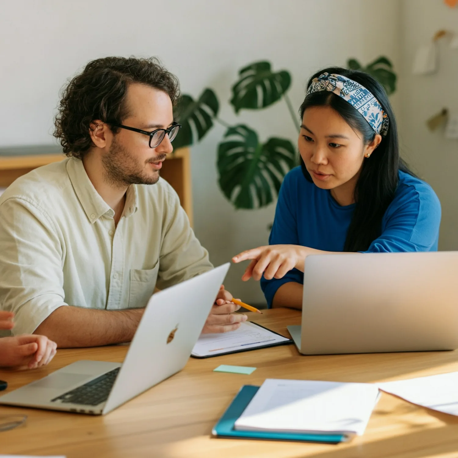 Two colleagues working side by side at laptops in a bright room with plants