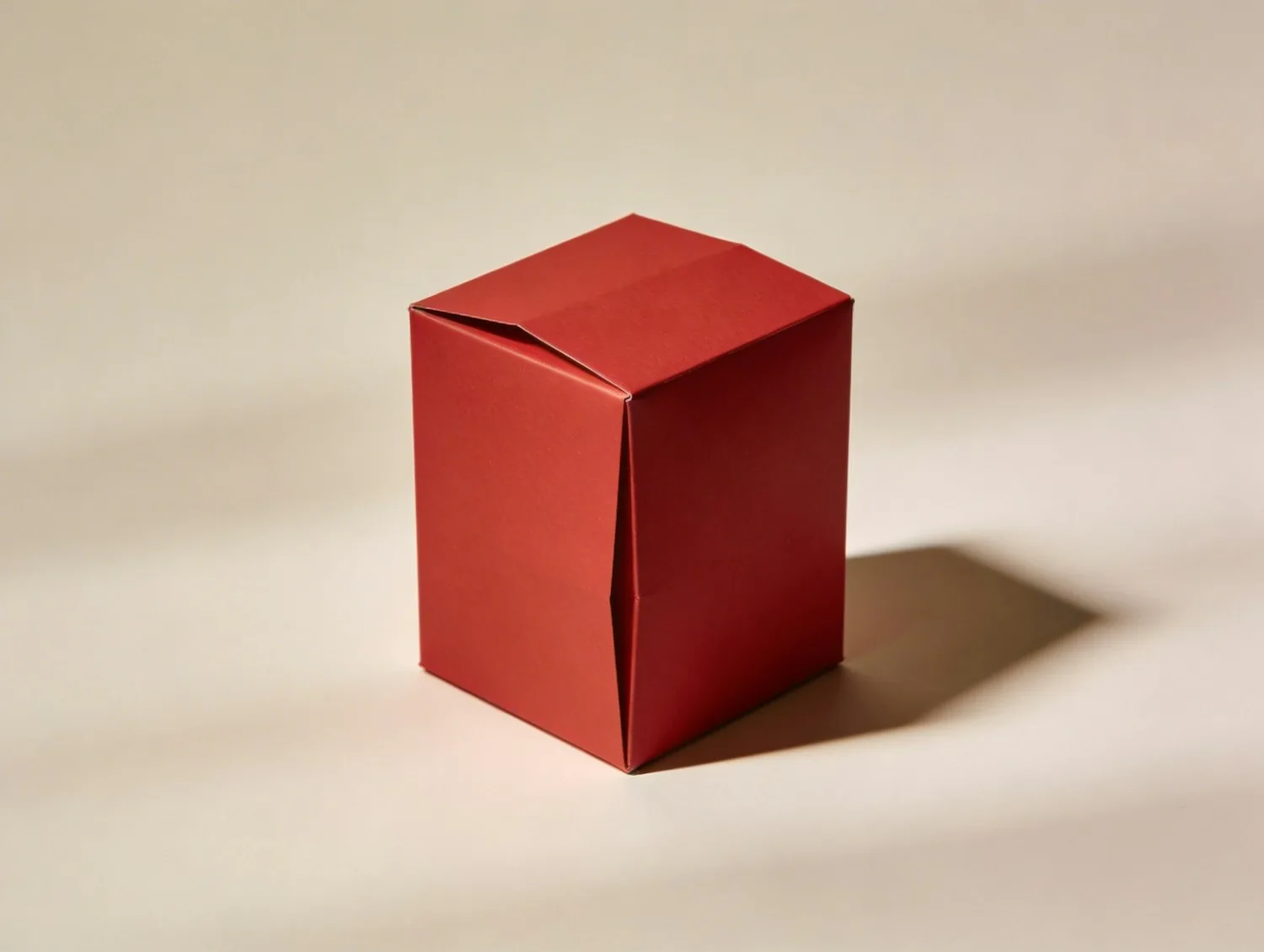 A single red paper box on a plain beige surface, lit from the side